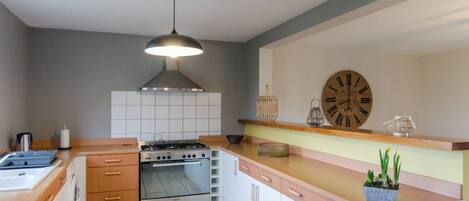 A modern kitchen with a gas stove, oven, and a large clock on the wall.