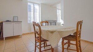 Un coin repas comprenant une table ronde, quatre chaises en bois, un buffet blanc et une fenêtre donnant sur l’extérieur.