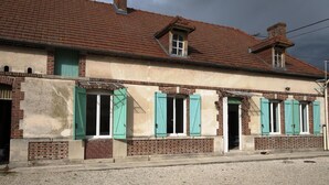 Un bâtiment à deux étages avec une façade en briques, de nombreuses fenêtres dotées de volets verts et un toit recouvert de tuiles.