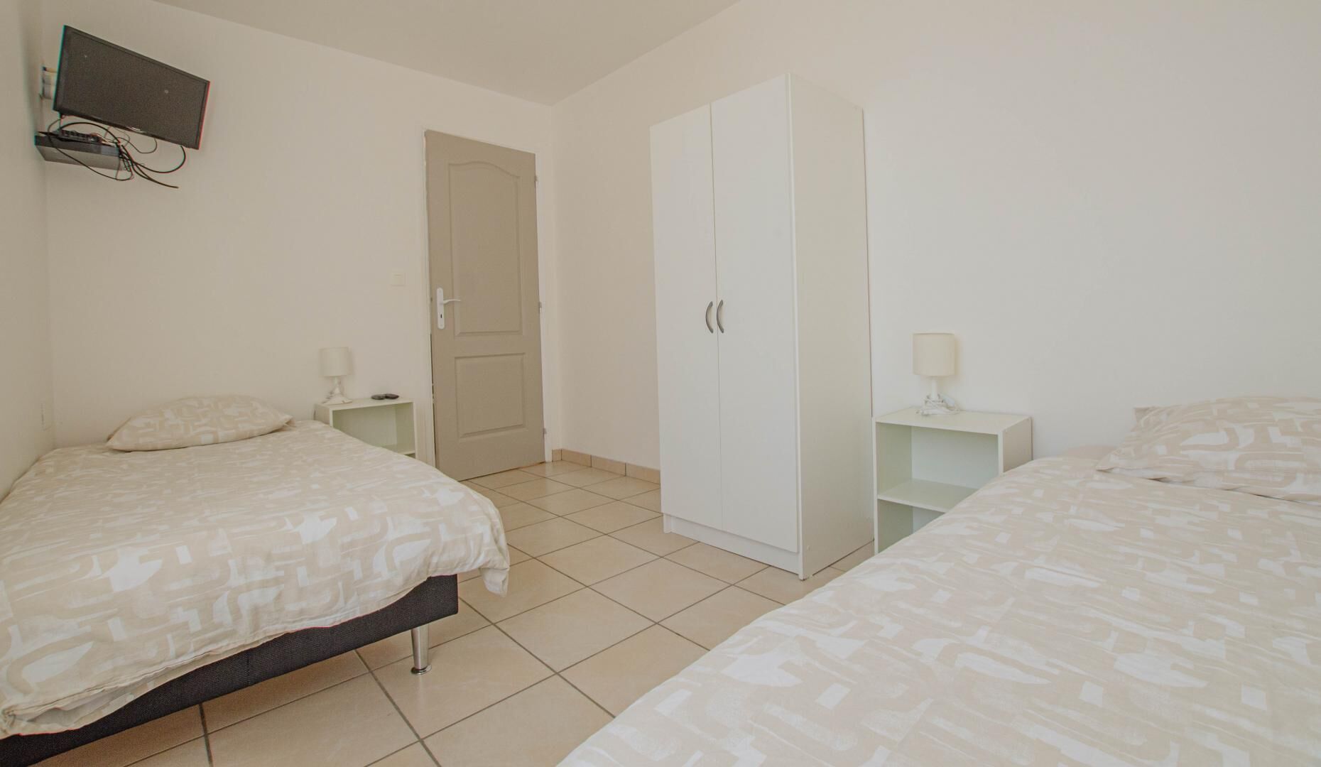 Un dormitorio con dos camas, un armario, un televisor montado en la pared y una puerta.