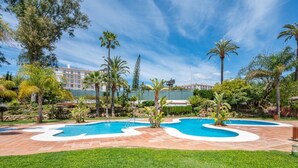 A pool area with a curved design, surrounded by palm trees and a well-maintained lawn. - Studio in Medina Garden for 2 people | 322 (Puerto Banús - Marbella)