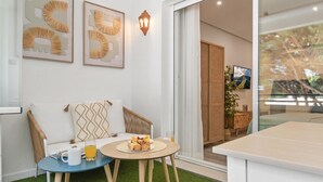 A modern room with a sofa, two chairs, a small round table with a plate of pastries and a glass of orange juice, and a large window with a view of trees. - Studio in Medina Garden for 2 people | 322 (Puerto Banús - Marbella)
