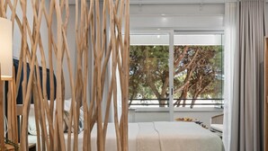 A modern hotel room with a large window, a bed with a white and beige blanket, and a wooden decorative screen. - Studio in Medina Garden for 2 people | 322 (Puerto Banús - Marbella)