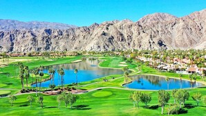 A golf course with multiple ponds, surrounded by mountains and residential areas.