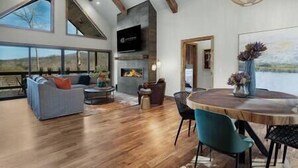 Uma sala de estar ampla com lareira, uma janela grande e um espaço de refeições com cadeiras e mesa.
