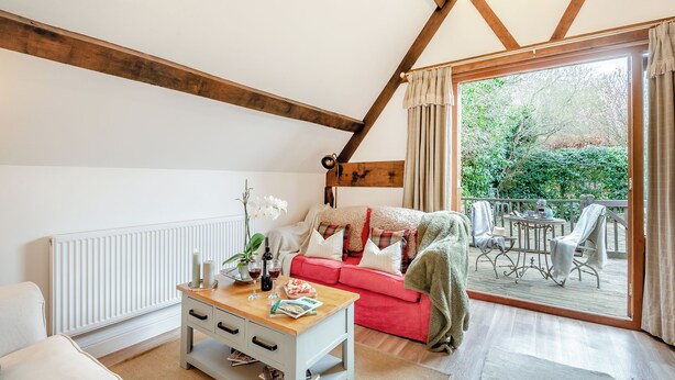 Un salon chaleureux avec un canapé rouge, une table basse en bois et une vue sur le jardin grâce à une porte vitrée.