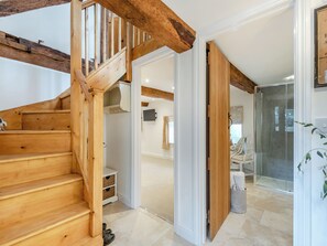 Una escalera de madera conduce a una habitación con una puerta blanca, zona de ducha de vidrio y una pared blanca con un televisor montado.