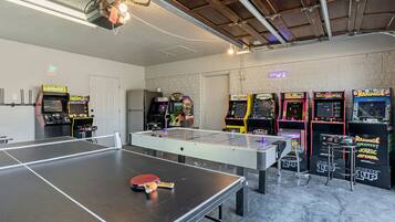 A room with a ping pong table, arcade games, and a neon sign.
