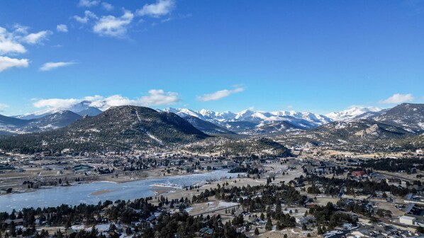 Une vue panoramique d’une ville, avec une rivière, des montagnes et des sommets enneigés en arrière-plan.