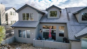 Une maison à deux étages avec un toit en pente, de grandes fenêtres et une terrasse clôturée.