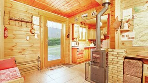 A wooden cabin interior with a kitchen, a fireplace, and a door leading to a balcony. - Le Chant de la Rivière - Chalet 3* pour 8 personnes (Ventron)