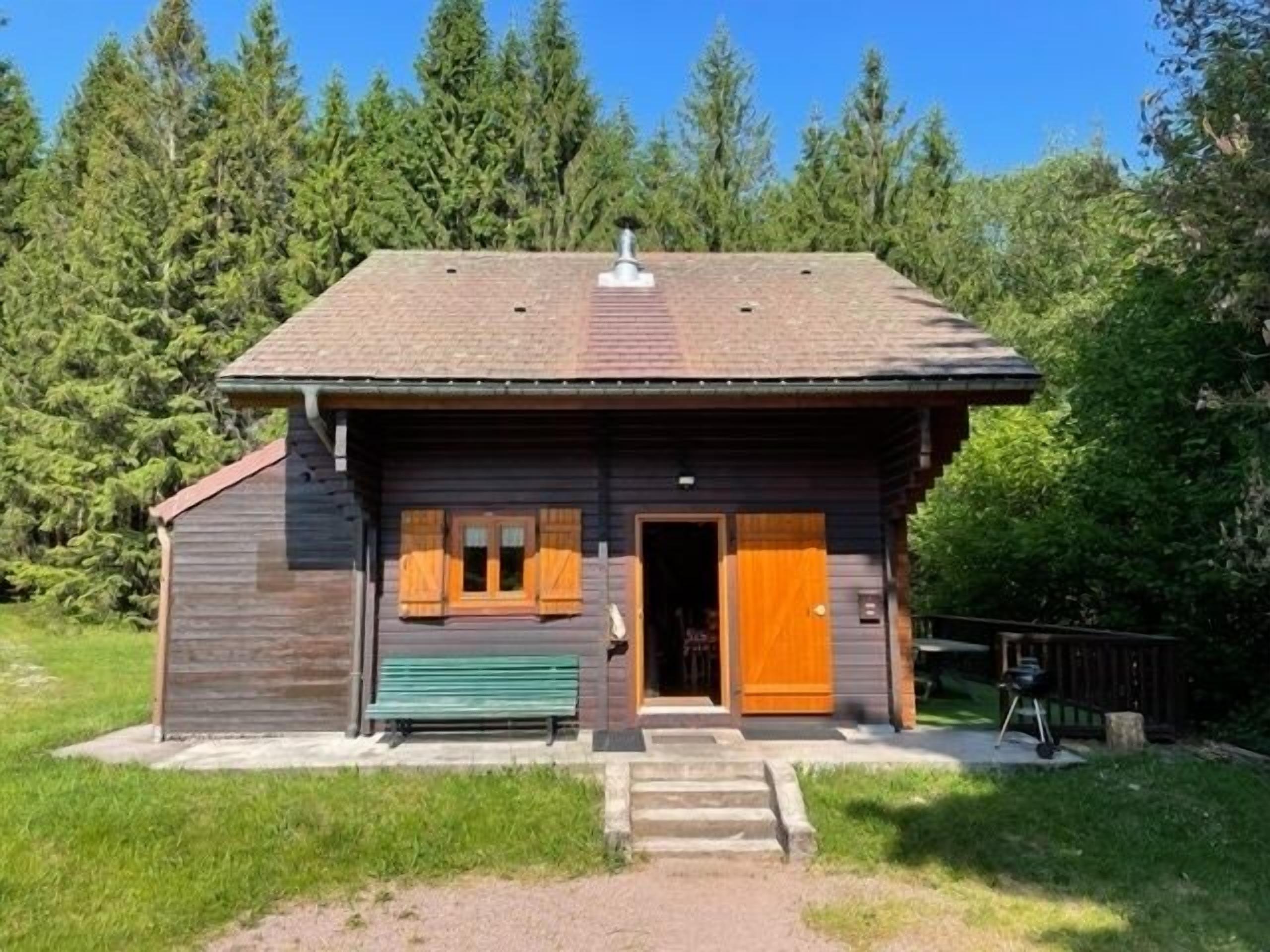A rustic cabin with a wooden exterior, a chimney, and a front door with wooden shutters.