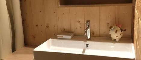 Bany d'una cabana de fusta amb un vàter blanc, un mirall i una petita estant amb un objecte decoratiu.