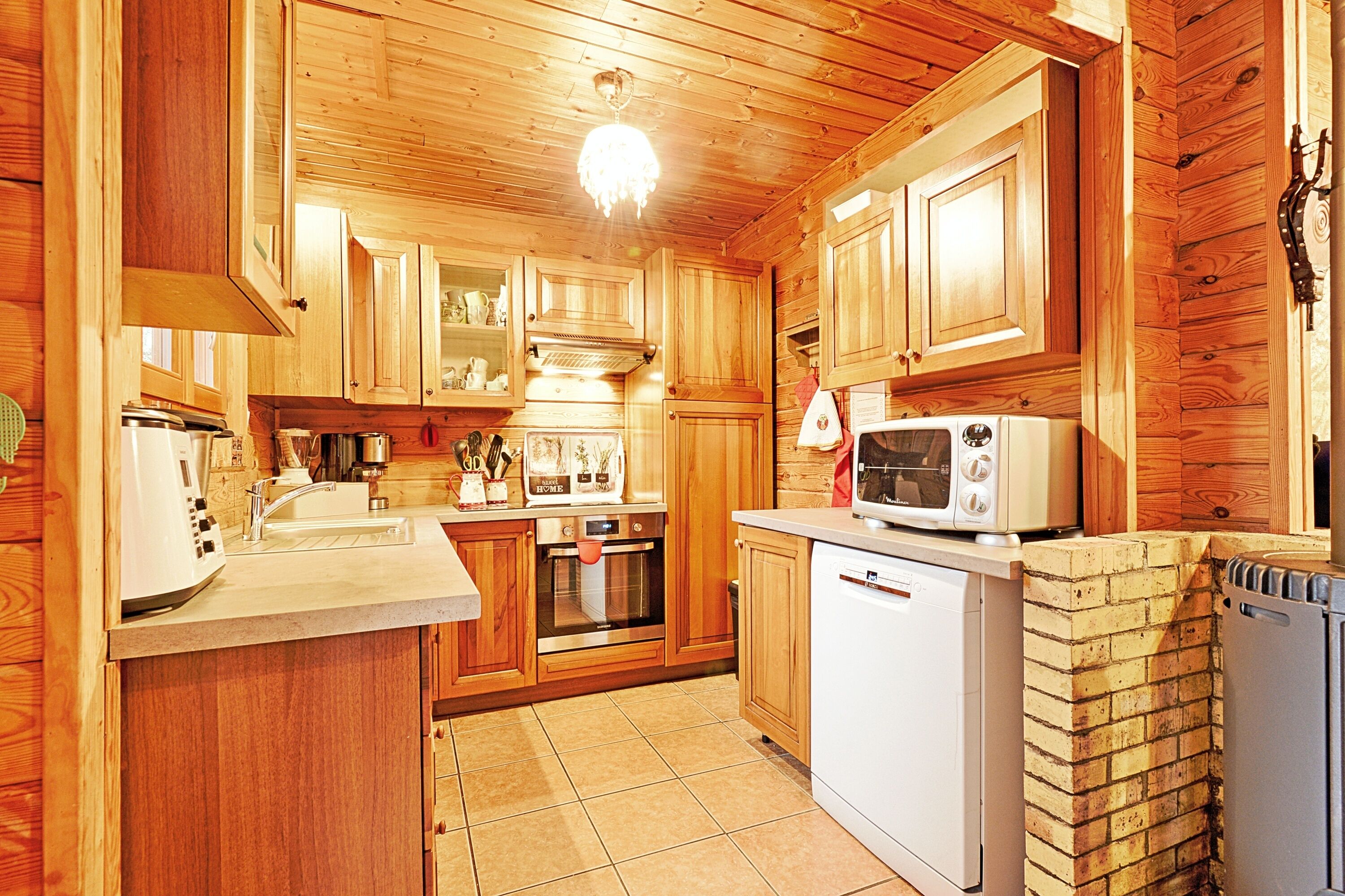 Een houten keukeninrichting in chaletstijl met een centraal eiland, een ingebouwde oven, een magnetron en een schouw van baksteen.