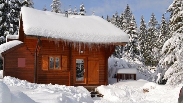 A wooden cabin with a snow-covered roof and a wooden door, surrounded by snow-covered trees. - Le Chant de la Rivière - Chalet 3* pour 8 personnes (Ventron)