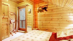 A wooden cabin bedroom with a bed, a wooden wardrobe, and a window with a view of the outdoors. - Le Chant de la Rivière - Chalet 3* pour 8 personnes (Ventron)