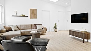 Moderni olohuone, jossa on sohva, nahkainen nojatuoli, sohvapöytä ja seinälle asennettu televisio.
