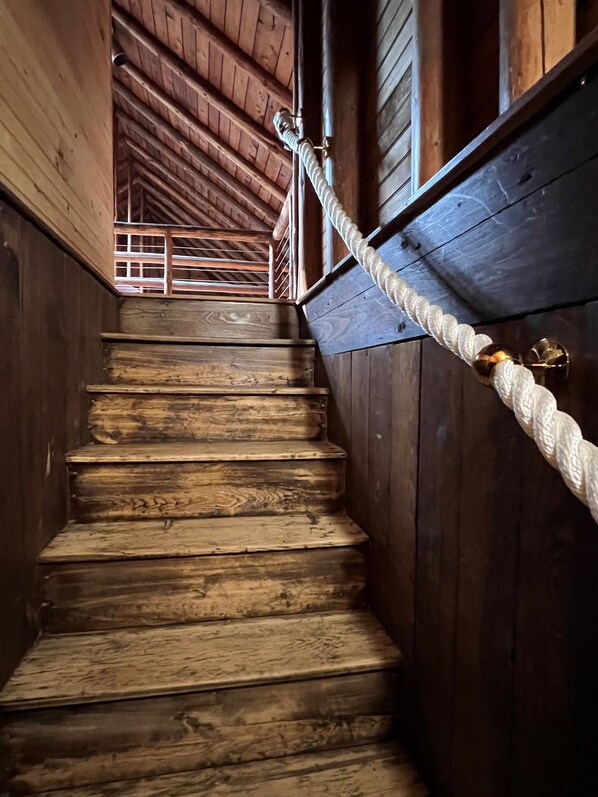 Un escalier en bois avec une main courante en corde, menant à une porte dotée d’un loquet métallique.