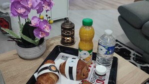 Un plateau contenant des aliments, une bouteille de jus, une bouteille d’eau et une bougie décorative, le tout posé sur une table en bois dans un salon.
