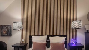 Une chambre d’hôtel avec un lit, deux tables de chevet, une lampe fixée au mur et un luminaire au plafond.