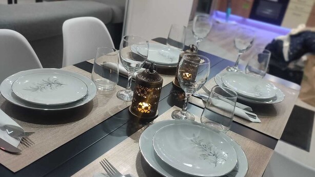 Un coin repas avec une longue table dressée pour quatre personnes, agrémenté d’assiettes blanches, de verres transparents et d’un chandelier servant de centre de table.