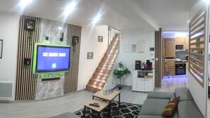 Un salon moderne doté d’un téléviseur à écran plat, d’un escalier, d’un coin cuisine et d’un espace repas.