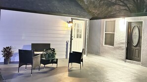Een terras buiten met twee stoelen, een tafel, een deur en een muur met een structuurafwerking.