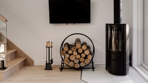 A modern living room with a TV mounted on the wall, a wood log storage rack, a fireplace, and a staircase.