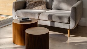 A modern living room with a grey sofa, two round wooden side tables, and a hanging woven light fixture.