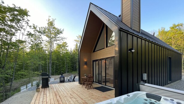 A modern cabin with a hot tub, deck, and outdoor seating area.
