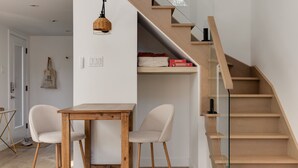 A modern interior with a wooden staircase, a dining area with two chairs and a table, and a shelf with board games.