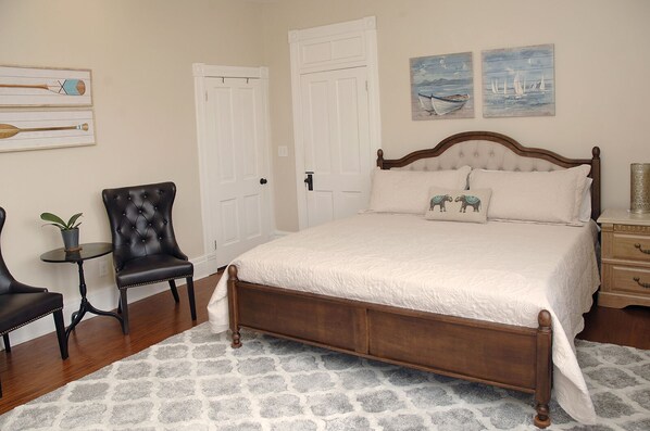 A bedroom with a large bed, two chairs, a small table, and artwork on the walls.
