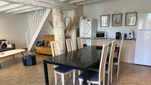 A dining area with a glass table and wooden chairs, a kitchen with appliances, a staircase, and a sofa. - T2 Climatisé Dans le Parc du Castel Silence, 900m de la Plage Port D'envaux (Port-d'Envaux)