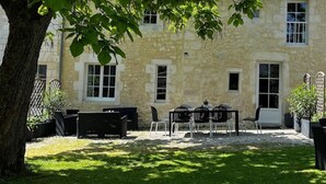 A stone building with a courtyard, outdoor seating, and a tree providing shade. - T2 Climatisé Dans le Parc du Castel Silence, 900m de la Plage Port D'envaux (Port-d'Envaux)