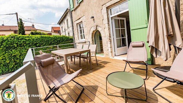 Un patio al aire libre con una mesa y sillas, una pequeña mesa redonda y un seto verde al fondo.