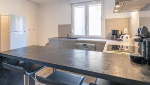 A modern kitchen with a central island, stainless steel appliances, and a window providing natural light. - L'appart' de la Goutte D'or (Avize)
