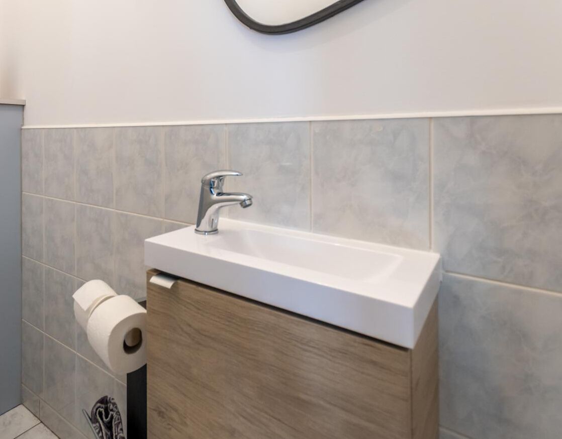 Ein Badezimmer mit einem weißen Waschbecken, einem Holzschrank darunter und einem Toilettenpapierhalter an der Wand.
