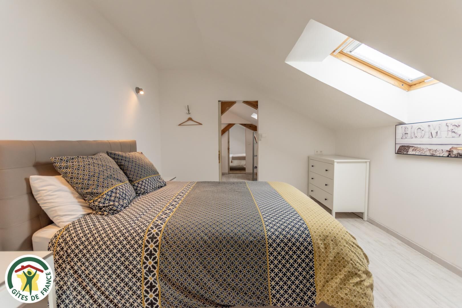 Een slaapkamer met een bed, een bureau, een kledingkast, een dakraam en een gang.