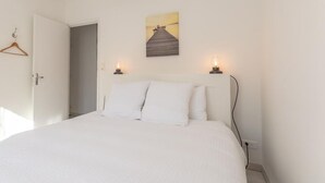 A bedroom with a bed, white walls, a door, a painting, and two wall-mounted lamps. - L'appart' de la Goutte D'or (Avize)