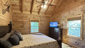 A wooden cabin bedroom with a bed, a dresser, a ceiling fan, and two windows. - Cozy Cabin Minutes to Helen and best hiking trails in the area! Pet Friendly! (Cleveland)