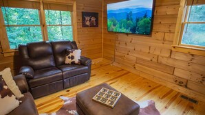 A wooden cabin interior with a leather sofa, a mounted TV, and a cowhide rug. - Cozy Cabin Minutes to Helen and best hiking trails in the area! Pet Friendly! (Cleveland)