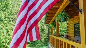 A wooden cabin with a porch, a hanging American flag, and a view of a forested area. - Cozy Cabin Minutes to Helen and best hiking trails in the area! Pet Friendly! (Cleveland)