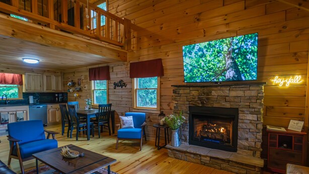 A cozy cabin interior with a stone fireplace, a television mounted above it, and a dining area with wooden furniture. - Cozy Cabin Minutes to Helen and best hiking trails in the area! Pet Friendly! (Cleveland)