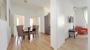 Een moderne woonkamer met een flatscreen televisie, een eethoek met een tafel en stoelen, en een keuken met een koelkast.
