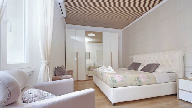 Een moderne slaapkamer met een groot bed, een stoel, een nachtkastje en een spiegel.