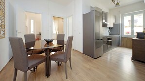 Een moderne keuken met roestvrijstalen apparatuur, een eethoek met een glazen tafel en vier stoelen, en uitzicht op het omliggende landschap door grote ramen.
