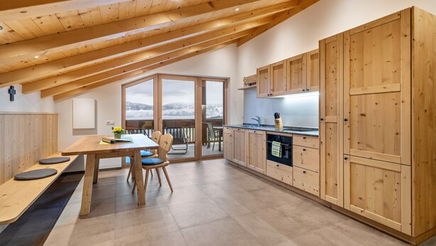 A modern kitchen with wooden cabinets, a dining area with a bench, and a view through a large window.