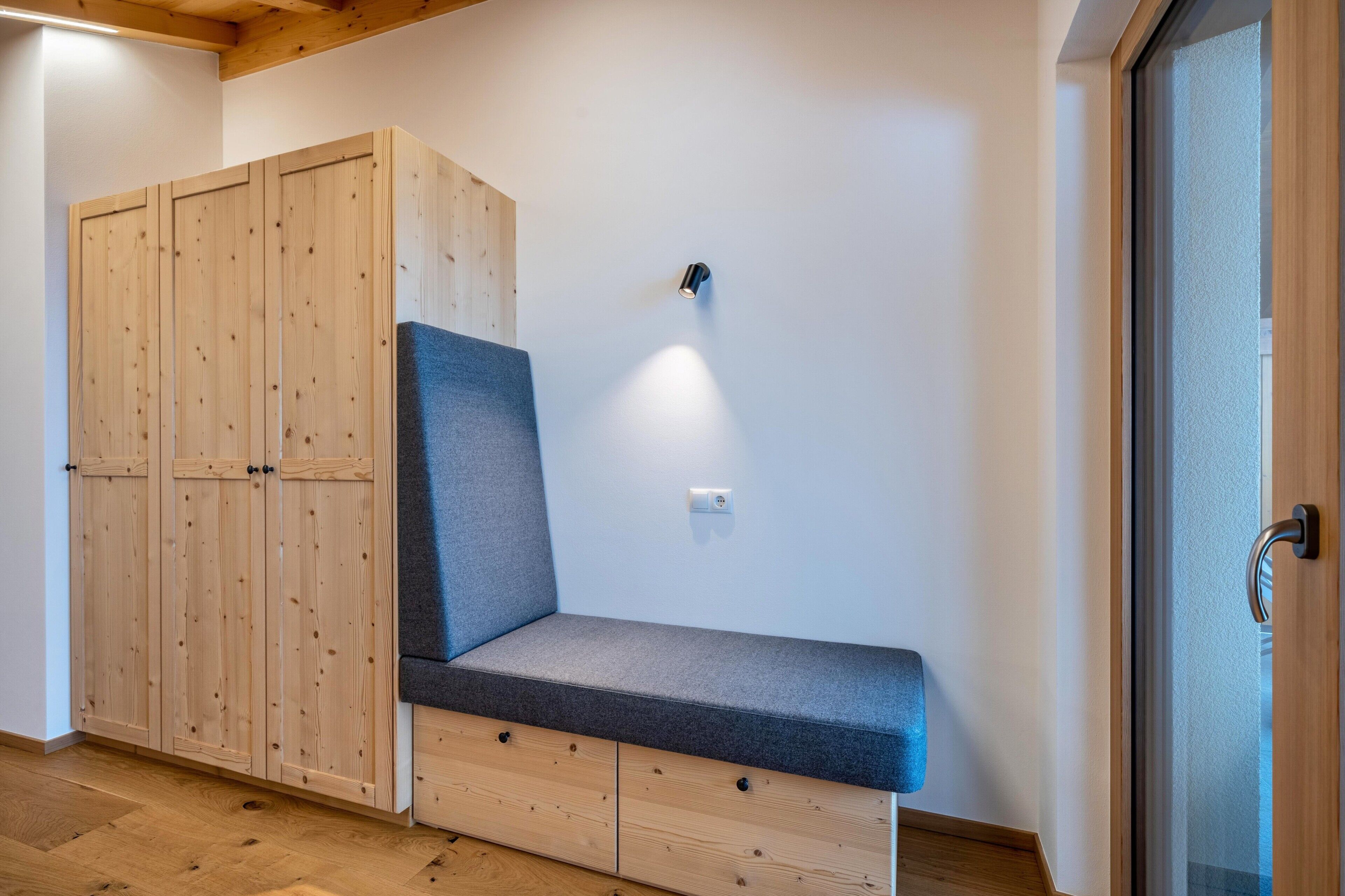 Een kamer met een inbouwkbank, een houten garderobe en een wandlamp.
