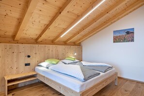 Un plafond en bois avec des poutres apparentes, un lit avec des oreillers, un petit banc en bois et un luminaire fixé au mur.