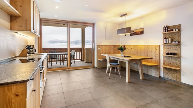 Une cuisine moderne avec des meubles en bois, un coin repas comprenant une table et des chaises, et une vue à travers une porte vitrée.
